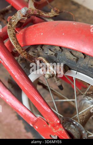 close-up of rusty rear wheel on red bicycle and brake mechanism with severe corrosion, soft focus on vintage transport decay concept in vertical Stock Photo