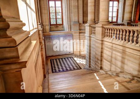 Stone staircase inside the Louvre Museum in Paris with an ornate painted ceiling arch above. Stock Photo