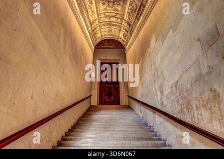 Stone staircase inside the Louvre Museum in Paris leading to a wooden door, with an ornate painted ceiling arch above. Stock Photo