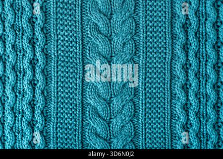 A closeup view of a teal knitted fabric showing thick braided cables and soft textured wool fibers. Christmas sweater background, top view. Stock Photo