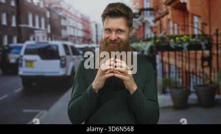 Young caucasian man with reddish beard and fingertips touching on urban street under daylight; confidence. Stock Photo