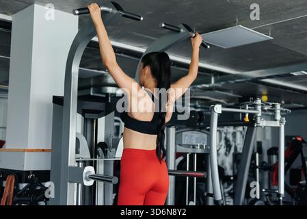 Muscular young woman doing pull up exercises on simulator Stock Photo