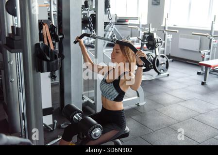 Muscular young woman doing pull up exercises on simulator Stock Photo