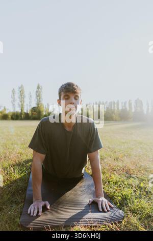 A man is doing a yoga pose on a mat in a field. Concept of calm and relaxation, as the man is focused on his breathing and posture Stock Photo