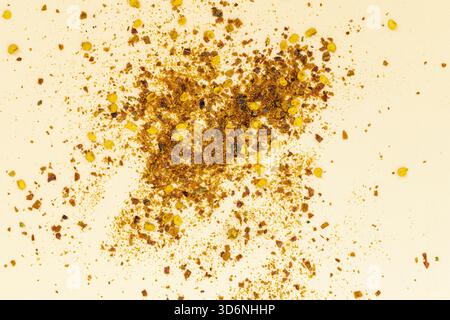 A close-up image of crushed chili pepper flakes and seeds scattered on a light beige surface, showcasing the vibrant red, orange, and yellow hues of t Stock Photo