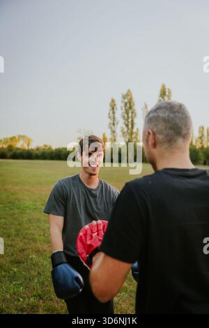 Two men training with boxing gloves in autumn park at sunset. Stock Photo