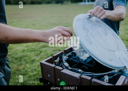 Man throwing empty plastic bottle in bin on green grass park in autumn. Stock Photo