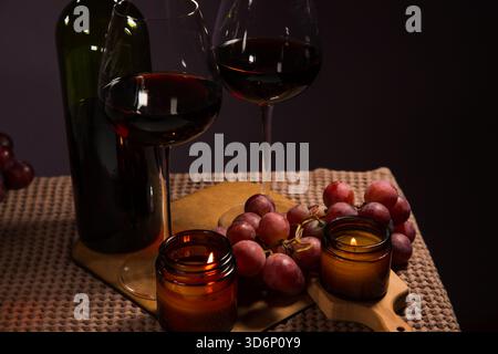 Still life two wine glasses with grapes bunch near romantic aroma burning flame fire candles on a table on dark background. Decor concept of Christmas Stock Photo