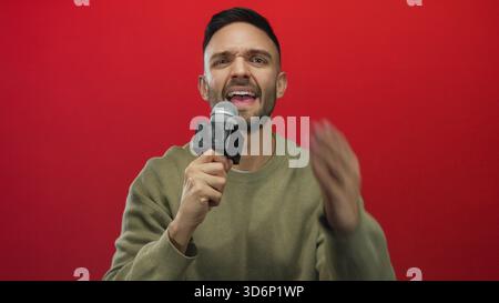 Young man with microphone giving an interview against red background showcasing expressive gestures and focused communication skills in a studio setti Stock Photo
