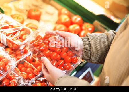 Hands holding a plastic container of bright red cherry tomatoes in the produce section of a grocery store or market. High quality photo Stock Photo