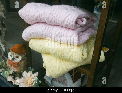 Two beautifully folded knitted blankets in pink and yellow attract attention from a small shop window in a quiet area. Stock Photo