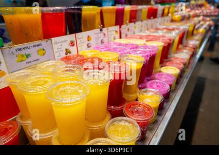 Colorful assortment of fresh fruit juices displayed in clear plastic cups at a market stall, featuring a variety of flavors and vibrant colors. Stock Photo