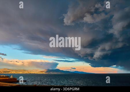 Dramatic Storm Clouds Over Calm Sea at Sunset Behind Mountain Horizon Stock Photo
