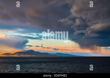 Dramatic Storm Clouds Over Calm Sea at Sunset Behind Mountain Horizon Stock Photo