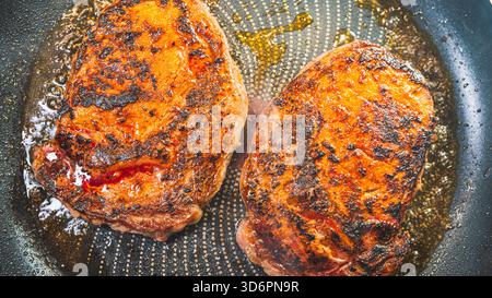 Ribeye steak sizzling in a pan, smoking and developing a golden crust while keeping juicy interior. Perfect for cooking tutorials and food content. Stock Photo
