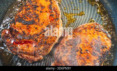 Ribeye steak sizzling in a pan, smoking and developing a golden crust while keeping juicy interior. Perfect for cooking tutorials and food content. Stock Photo