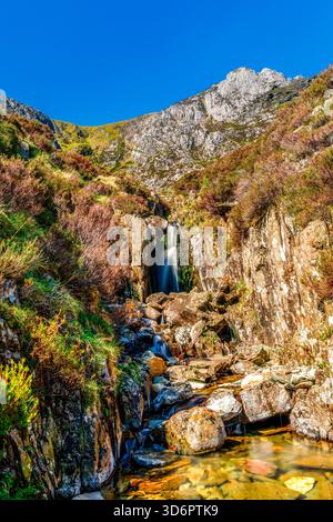 Mountain Waterfall Flowing Through Rocky Gorge Under a Bright Blue Sky in Snowdonia Stock Photo
