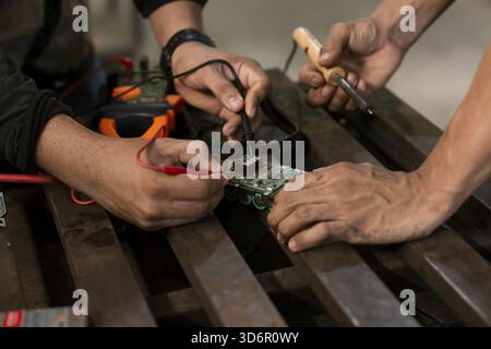 Close-up of two man using a soldering iron on an electronic circuit board on a table Stock Photo