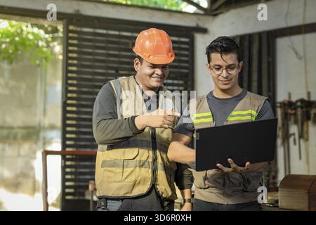 Carpentry foreman showing computer to colleague in the workshop. Carpentry Workshop manager using the computer to teach a worker Stock Photo