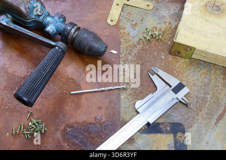 Vintage woodworking tools rusty table include old hand drill metal chuck black handle vernier caliper metal drill bit screws textured industrial feel Stock Photo