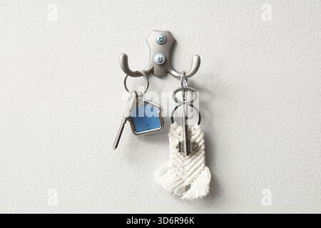 Keys from house hanging on hooks on light wall Stock Photo