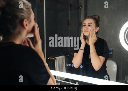 Young woman smiling, Casual woman in bathroom with moisturizer Stock Photo