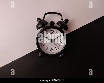 The small black analog alarm clock on a black and white background. Stock Photo
