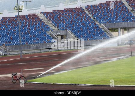 Serene scene of sprinkler watering green grass field in an empty stadium. irrigation system provides maintenance to track and field with empty seats i Stock Photo