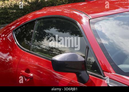 Close up view of modern red sports car coupe. shiny, sleek vehicle shows its aerodynamic exterior design, reflecting sky and conveying sense of speed Stock Photo