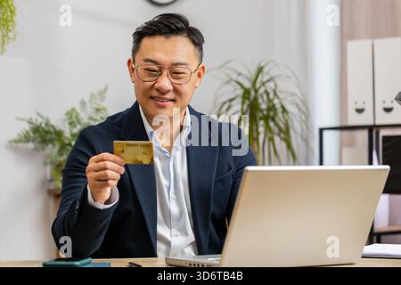Chinese businessman programmer software developer working making online purchase payment shopping with credit bank card and use laptop at home office desk with laptop. Asian freelancer business man Stock Photo