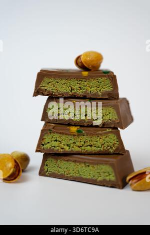 Vertical stack of chocolate bars with pistachio filling and whole nuts on top. Stylish food photography for dessert and snack themes.  Stock Photo