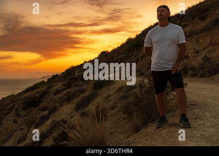 Hiker looks up at the glorious sunset sky on a mountain trail, feeling inspired and free. Stock Photo