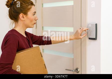 Profile view of female customer with parcel entering code on door lock at pickup Stock Photo
