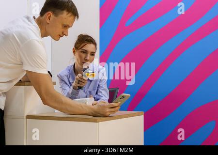 Female worker using scanner on male customer's smartphone at order collection counter Stock Photo