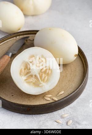 Unique heirloom Crystal Apple (Cucumis sativus) cucumber is shown sliced open, displaying its crisp interior on a rustic plate. Stock Photo