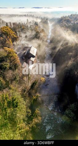 Autumn morning mist rising from the River Ericht in Blairgowrie, with warm sunlight streaming through the trees and old mill buildings along the river Stock Photo