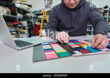 Fashion designer working with fabric swatches and laptop, selecting color samples for new collection. This image is ideal for illustrating the textile industry, creative process, and fashion design concepts. || Model released Stock Photo