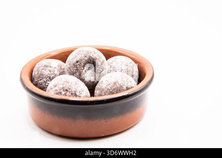 Chocolate truffles arranged in a small earthenware dish on a plain background, suitable for dessert and confectionery themes. Stock Photo