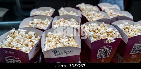 Documentary close-up of fresh popcorn served in branded cardboard boxes arranged at an indoor snack counter in a recreational facility. Stock Photo