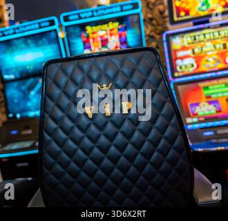 Close-up of a VIP leather chair inside a casino, with quilted texture, gold lettering and colorful slot machines blurred in the background. Stock Photo
