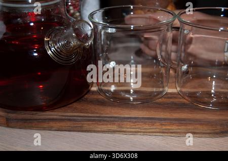 A glass kettle with black tea and two empty glass mugs. Tea mugs and a teakettle on the wooden table. Stock Photo