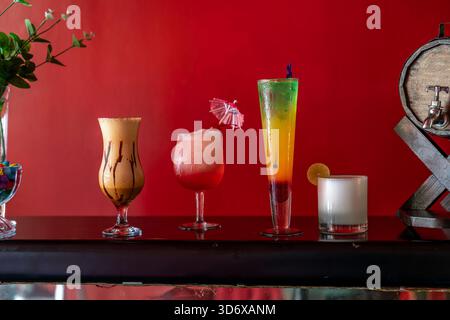 Colorful cocktails arranged on a bar against a vibrant red background, showcasing refreshing mixed drinks and stylish glassware. Stock Photo