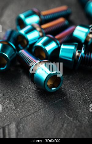 A collection of titanium blue hexagonal head screws against a dark textured backdrop, captured in close-up Stock Photo