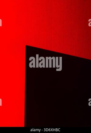 Abstract composition featuring a dark, geometric shadow casting across a vibrant red background, highlighting the interplay of light and creating a st Stock Photo