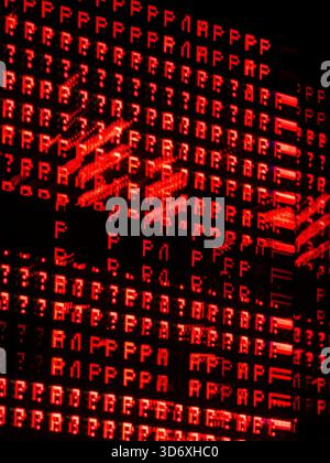 Red digital text and symbols forming an abstract pixelated data background, showing glitches and errors on a dark screen representing cybersecurity, h Stock Photo