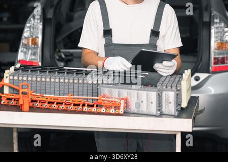 Serviceman repairs electric battery pack of hybrid car using digital tablet Stock Photo