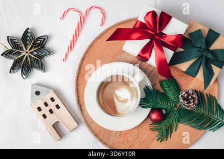 A cup of coffee on a wooden tray surrounded by bright ornaments, gift boxes, ribbons, pine cone and evergreen branch. Christmas holiday concept. Top v Stock Photo