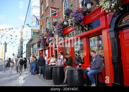 People enjoy drinks outside the vibrant red facade of The Ferryman Townhouse pub on Sir John Rogerson's Quay in Dublin, Ireland. Stock Photo