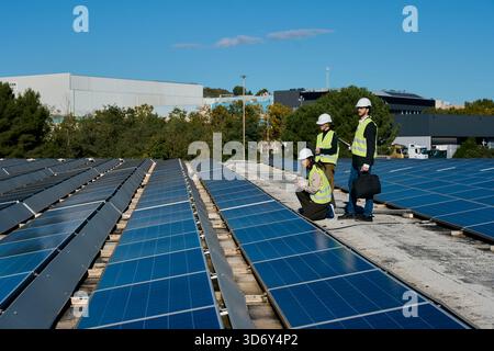 Engineers inspecting solar panels on factory rooftop Stock Photo