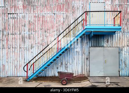 Wall of an old industrial building with stairs and a wheelbarrow. Stock Photo